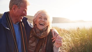 En glad eldre mann og kvinne i solnedgang ved kysten