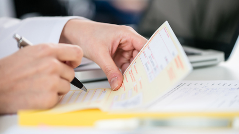 Illustrasjonsbilde som viser et nærbilde av et par hender som skriver ut en resept