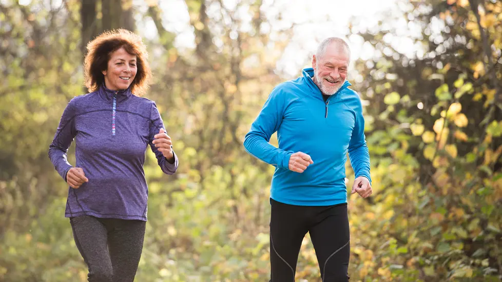 En eldre mann jogger i naturen sammen med en middelaldrende kvinne