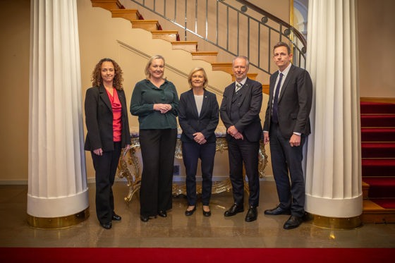 Tre kvinner og to menn poserer mellom to søyler og foran en trapp