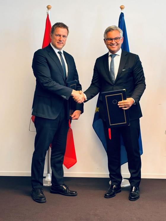 Statssekretær Øren trykker EU-kommisær Magnus Brunner i hånda foran det norske og EU-flagget