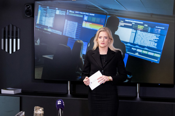 Statsråden taler foran en stor skjerm med illustrasjoner relatert til datasikkerhet.