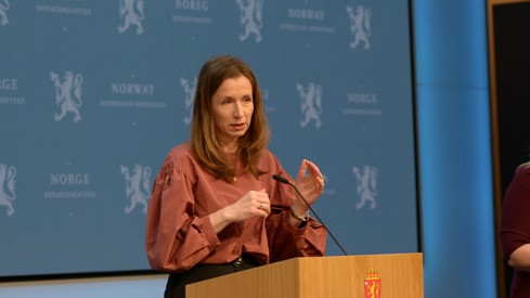 Justisministeren på talestol foran regjeringens blå pressevegg.