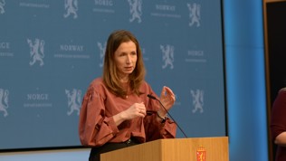 Justisministeren på talestol foran regjeringens blå pressevegg.