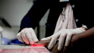 Person having their finger scanned by a woman with white gloves