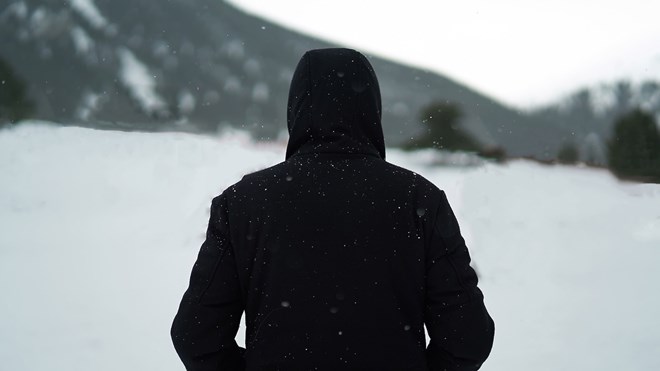 Person med svart hettegenser med ryggen til i snødekt landskap.