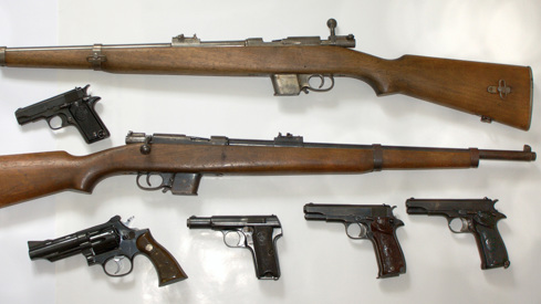 En samling av gamle rifler og pistoler som ligger på et hvitt bord.