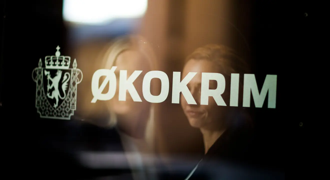 Refleksjon av to kvinner med lyst hår i et vinduet. På vinduet står det «Økokrim» med store hvite bokstaver.