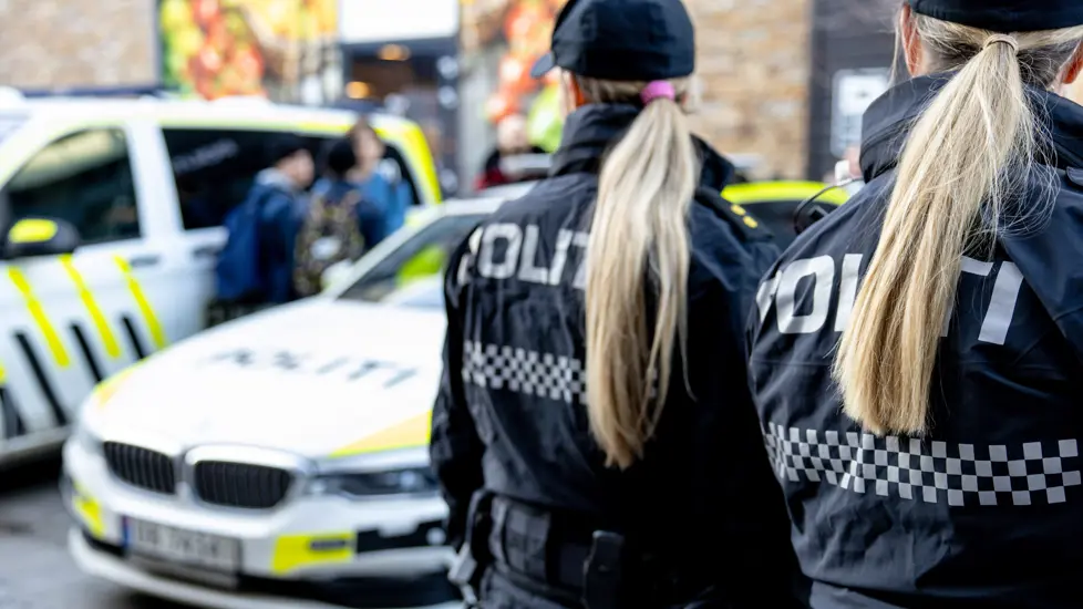 To kvinner i politiuniform med ryggen til. To politibilder står i bakgrunnen.