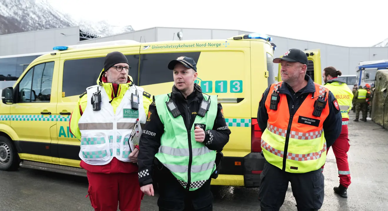 En ambulansearbeider og to politibetjenter foran en ambulanse.