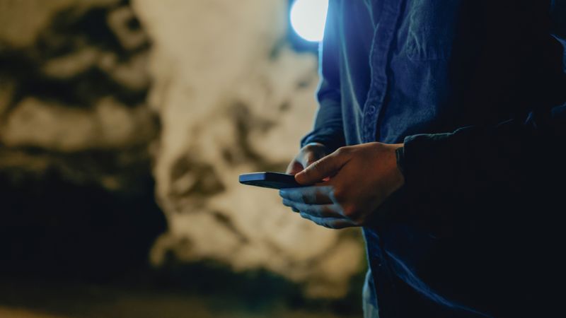 Person holder smarttelefon i hånda i mørke omgivelser.