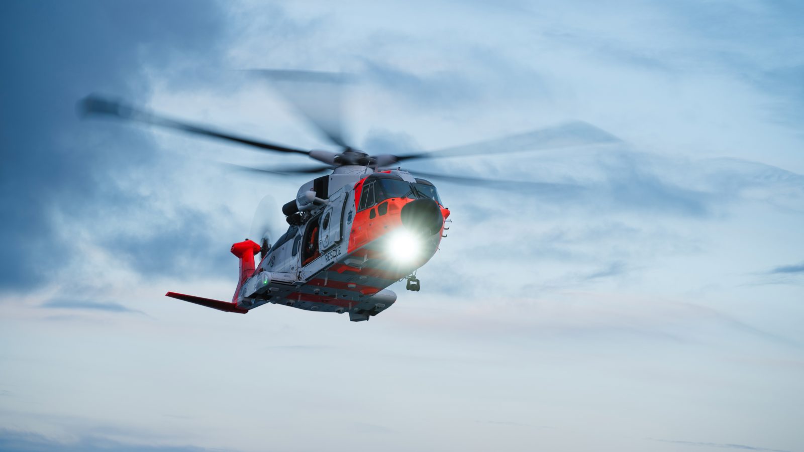 Oransje og hvitt SAR Queen-redningshelikopter flyr i skumringen