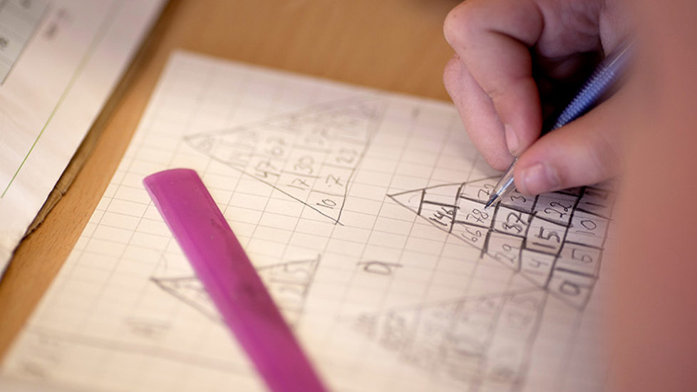 Bilde av et ark med regnestykker og hånd med blyant