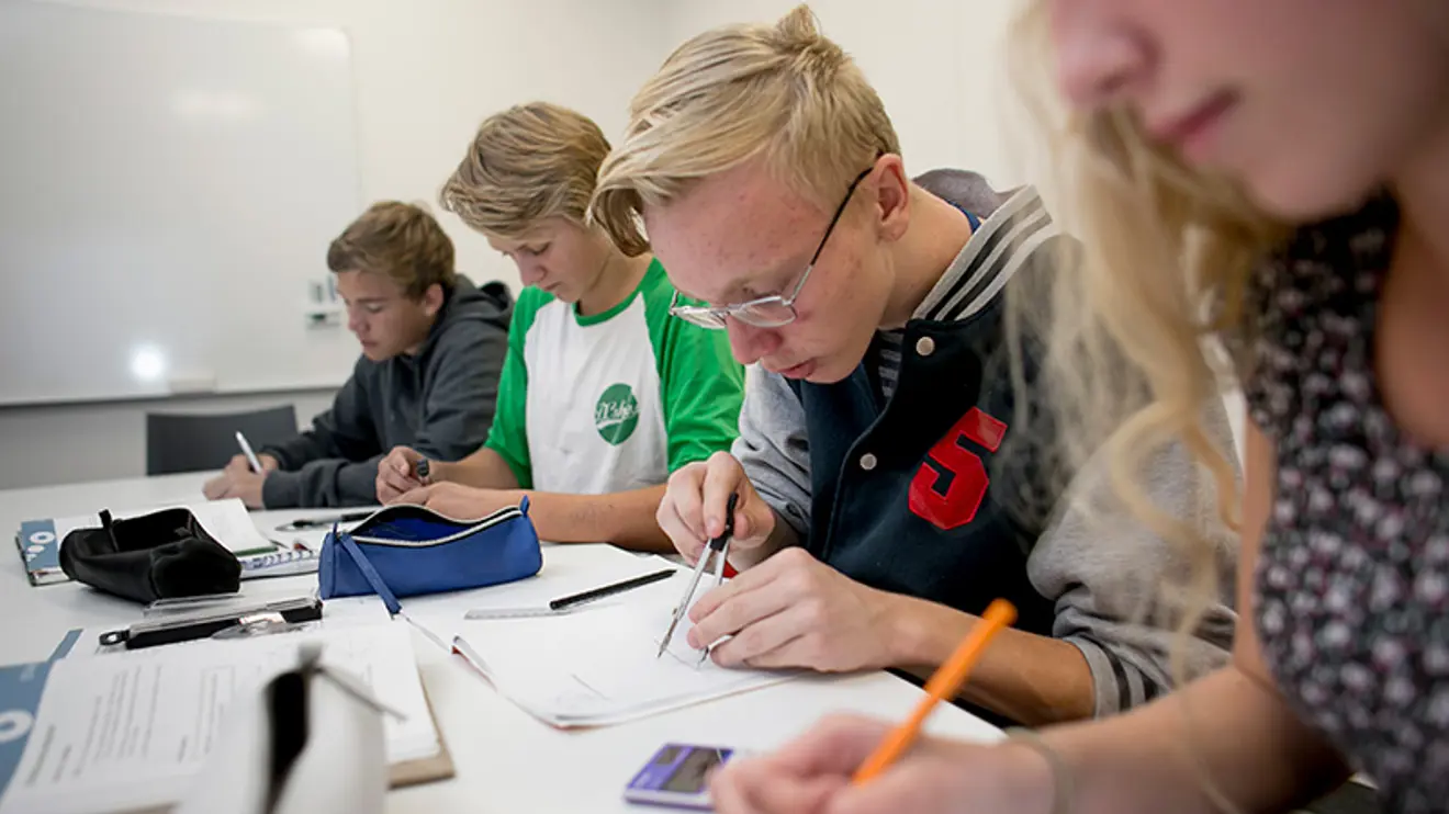 Bilde av fire elever som sitter på rekke og jobber med matematikk 