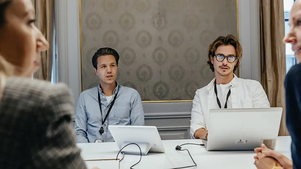 Bilde av fire personer i møte med PC-er foran seg.