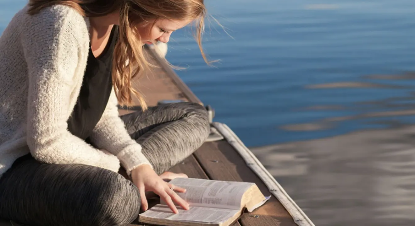 Kvinne som sitter på brygga og leser en bok