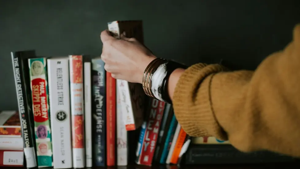 Illustrasjonsbilde av en hånd som tar ut en bok fra en bokhylle.