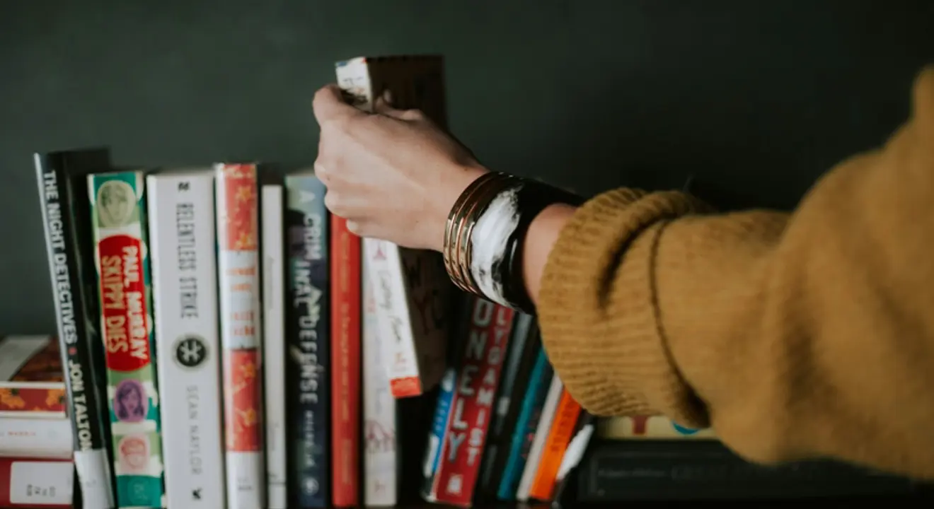 Illustrasjonsbilde av en hånd som tar ut en bok fra en bokhylle.