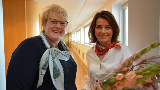 Statsråd Trine Skei Grande og den nye NFI-direktøren Kjersti Mo  står ved siden av hvernadre. Mo holder i blomsterbukett.