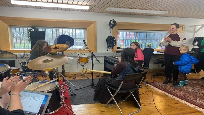 Tre unge jenter speler på trommer, bass og keyboard og kultur- og likestillingsministeren ser på