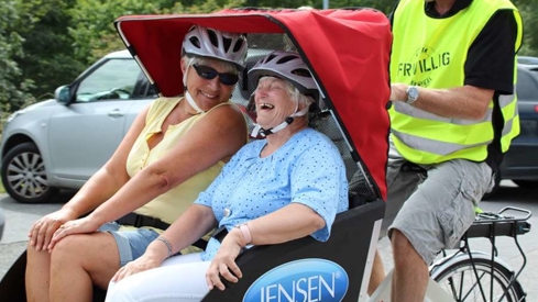 Frivillig som sykler en sykkelvogn med to voksne passasjerer.