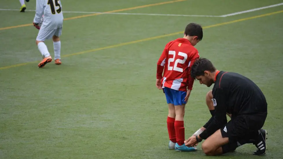 Illustrasjonsbilde: Mann hjelper gutt å knyte lisser på fotballskoene. Foto: Adrià Crehuet Cano / Unsplash