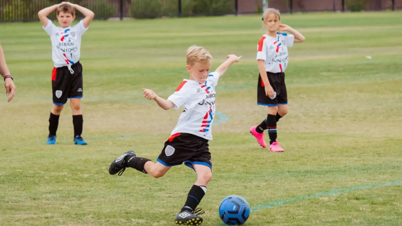 Tre barn spiller fotball på fotballbane