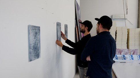 Kunstneren Javier Barrios og en annen mann henger opp et kunstverk på veggen.