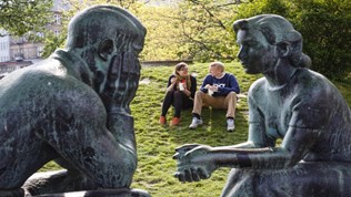 Mann og kvinne sitter i en park, med statuer foran seg