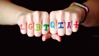 Illustrasjonsbilde av to knyttede hender med bokstavene LGBTQIA+ malt på fingrene