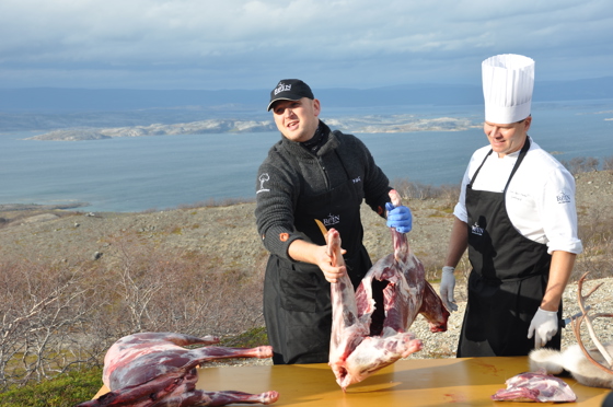 Landbruks- og matminister Jon Georg Dale og Svein Jæger Hansen parterer reinkjøtt med Porsangerfjorden i bakgrunnen.