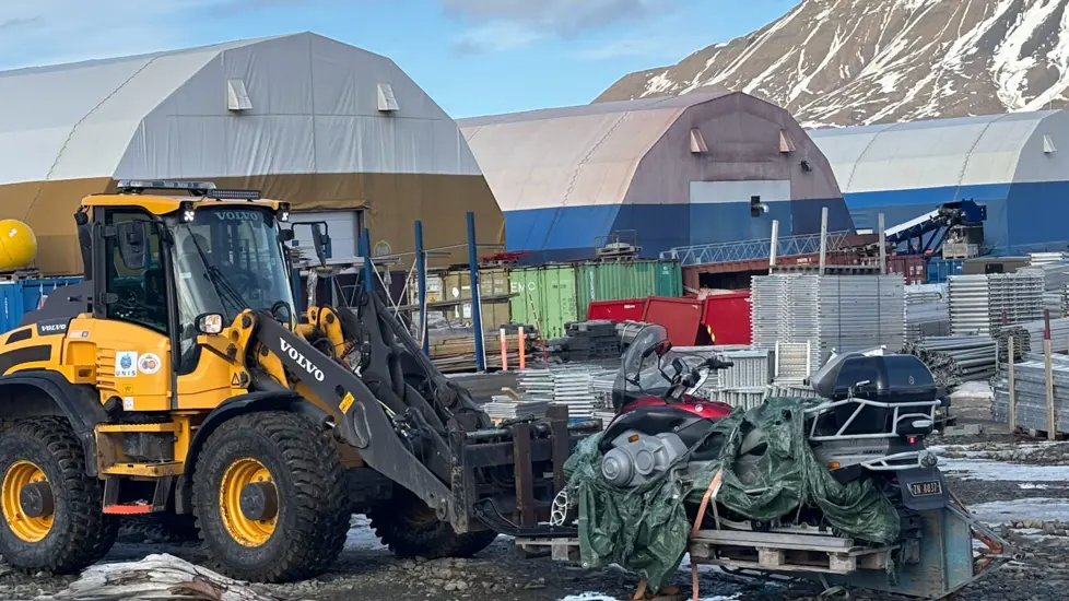 Gul traktor løfter en snøskuter som står på en pall
