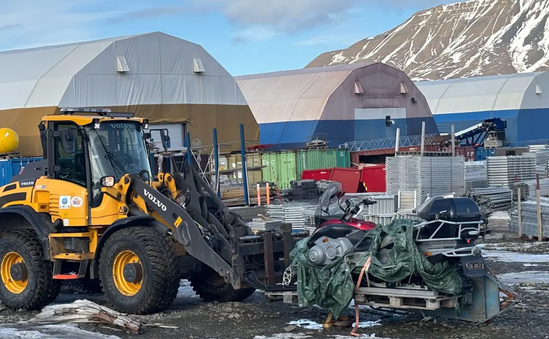 Gul traktor løfter en snøskuter som står på en pall