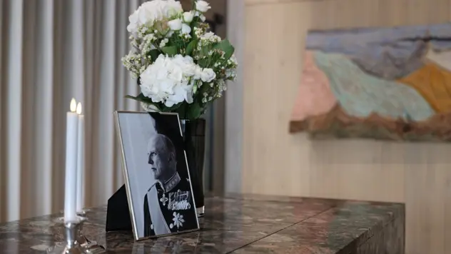 Lys, portrettbilde av Kong Harald V og blomster på en steinbenk.
