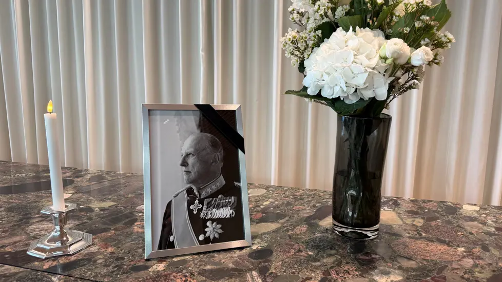 Lys, portrettbilde av Kong Harald V og blomster på en steinbenk.
