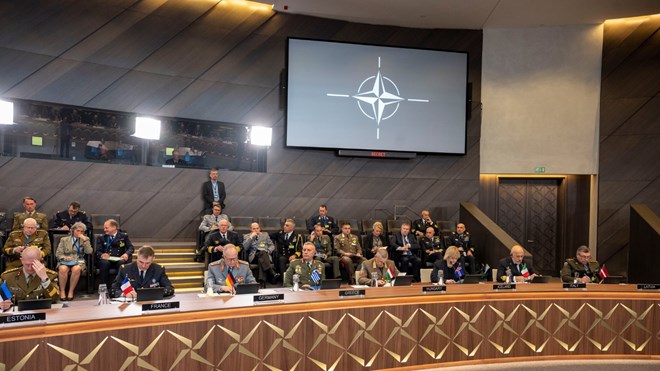 Fra et av møterommene i NATO. Bildet viser noen av medlemslandene, representert ved forsvarssjefer som sitter på hver sin plass rund et ovalt bord, med flagget til landet de representerer foran seg.