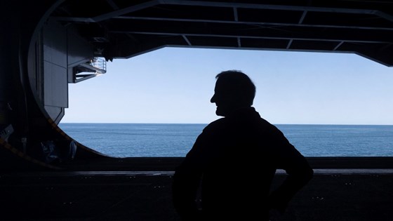 Statsminister Jonas Gahr Støre i svart silhuett mot blå himmel på hangarskipet USS Gerald R. Ford.