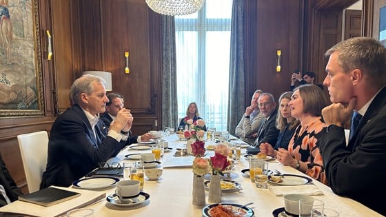 Statsminister Jonas Gahr Støre møter forskere. Sitter ved et langt møtebord som er dekket til frokost.