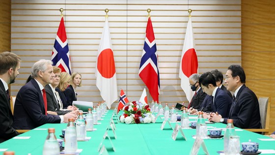Møtebord med statsministrene fra Norge og Japan sammen med delegasjonene deres på hver side av bordet. Japanske og norske flagg i bakgrunnen.