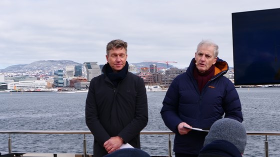 Olje- og energiminister Tejre Aasland og statsminister Jonas Gahr Støre stor på dekket av en båt med Bjørvika i Oslo i bakgrunnen.
