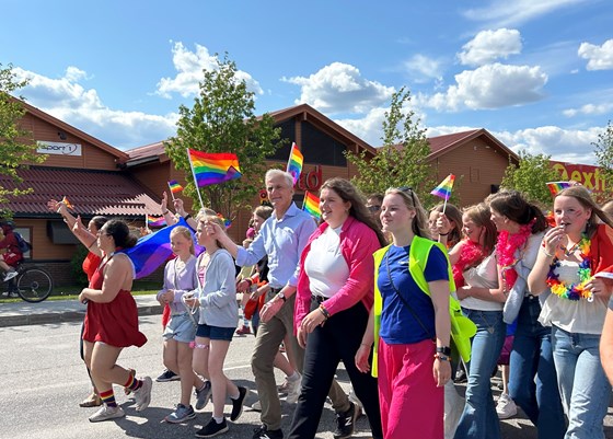 Statsminister Jonas Gahr Støre går i prideparade på Tynset sammen med arrangørene av festivalen. Han holder et regnbueflagg i hånden.