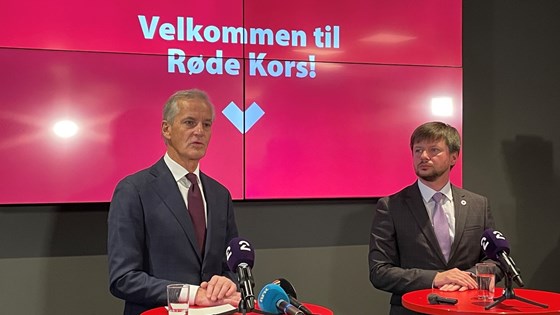 Jonas Gahr Støre og Kors Maksym Dotsenko holder pressekonferanse og står ved hvert sitt bord foran en bakvegg med teksten Velkommen til Røde Kors.