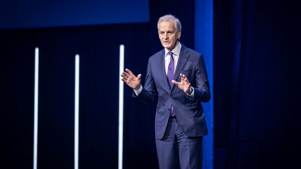 Statsminister Jonas Gahr Støre står på scenen i Oslo Spektrum. Dress med lilla slips. 