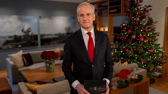 Statsministeren står ved juletreet i statsministerboligen. Mørk dress og rødt slips.