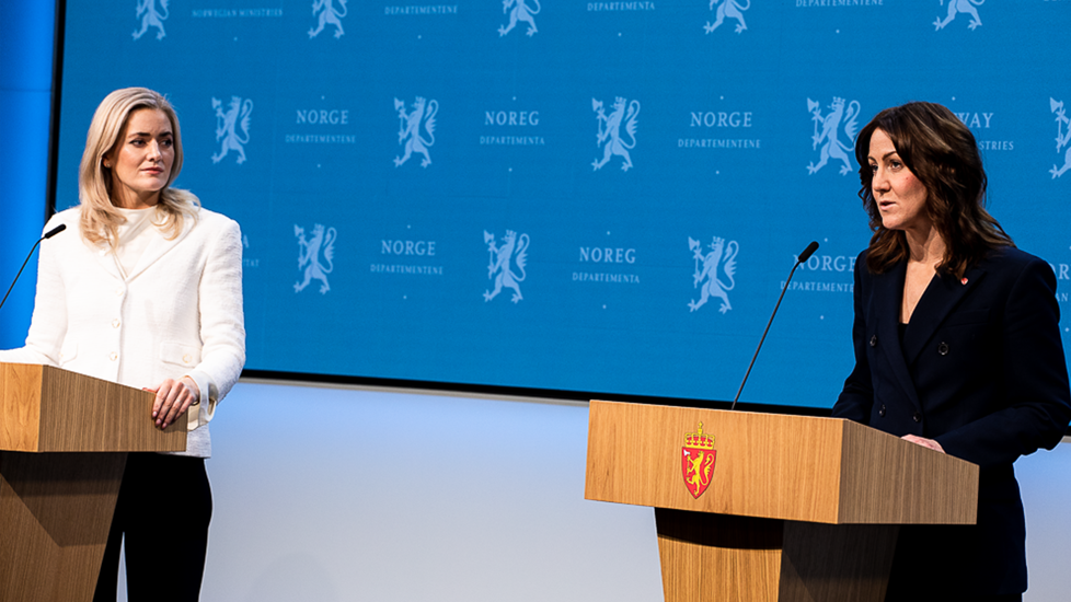 Justis- og beredskapsminister Emilie Enger Mehl og arbeids- og inkluderingsminister Tonje Brenna står foran en blåvegg på scenen i Marmorhallen.