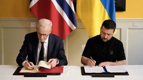 Prime Minister Jonas Gahr Støre and President Volodymyr Zelensky signing the agreement. Sitting at chairs behind a table.