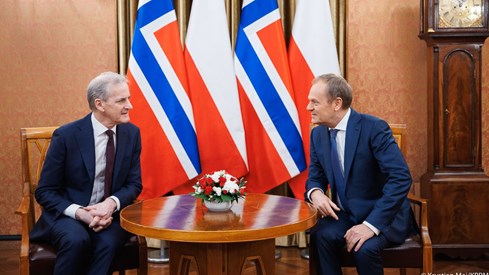 Støre og Tusk i samtale foran fire flagg, to norske og to polske. De to sitter i hver sin stol.