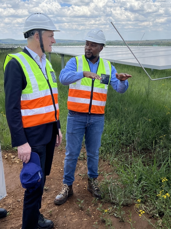Statsministeren besøker et solcelleanlegg. Ser på solcellepaneler og snakker med lokalt ansatt.