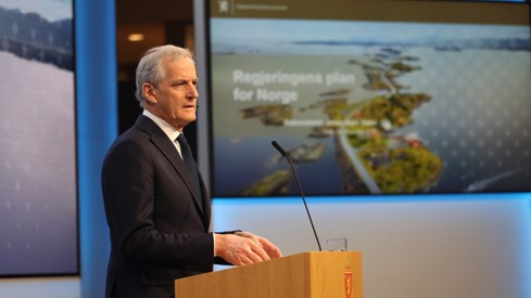 Statsministeren står på scenen i Marmorhallen. Bilde fra Atlanterhavsvegen i bakgrunnen.