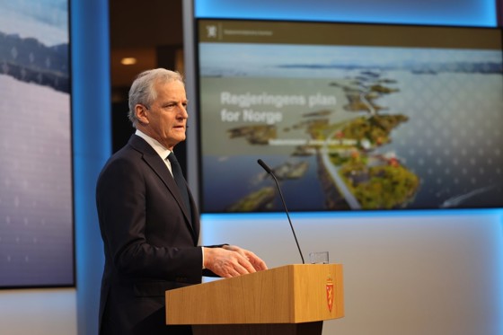 Statsministeren står på scenen i Marmorhallen. Bilde fra Atlanterhavsvegen i bakgrunnen.